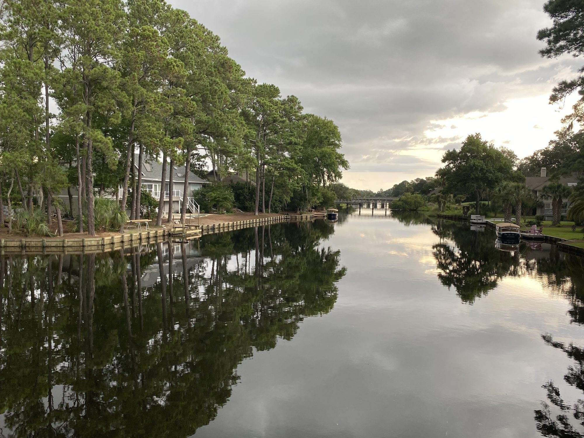Still water on the Palmetto Dunes lagoon, with pines, docks, and a bridge in the distance