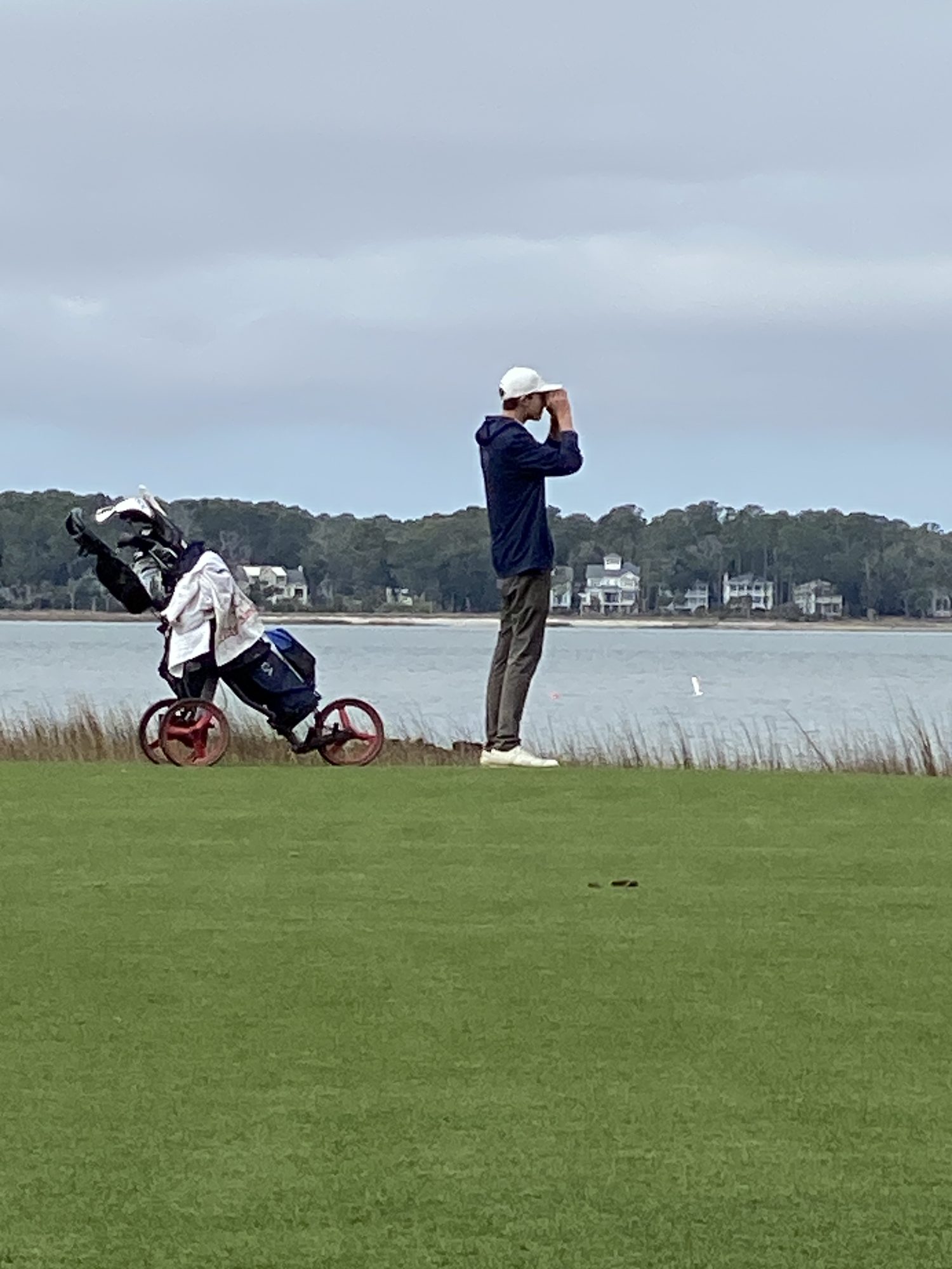 Junior player on the 18th at Harbour Town Golf Links, looking through a rangefinder toward the green, with Daufuskie Island beyond